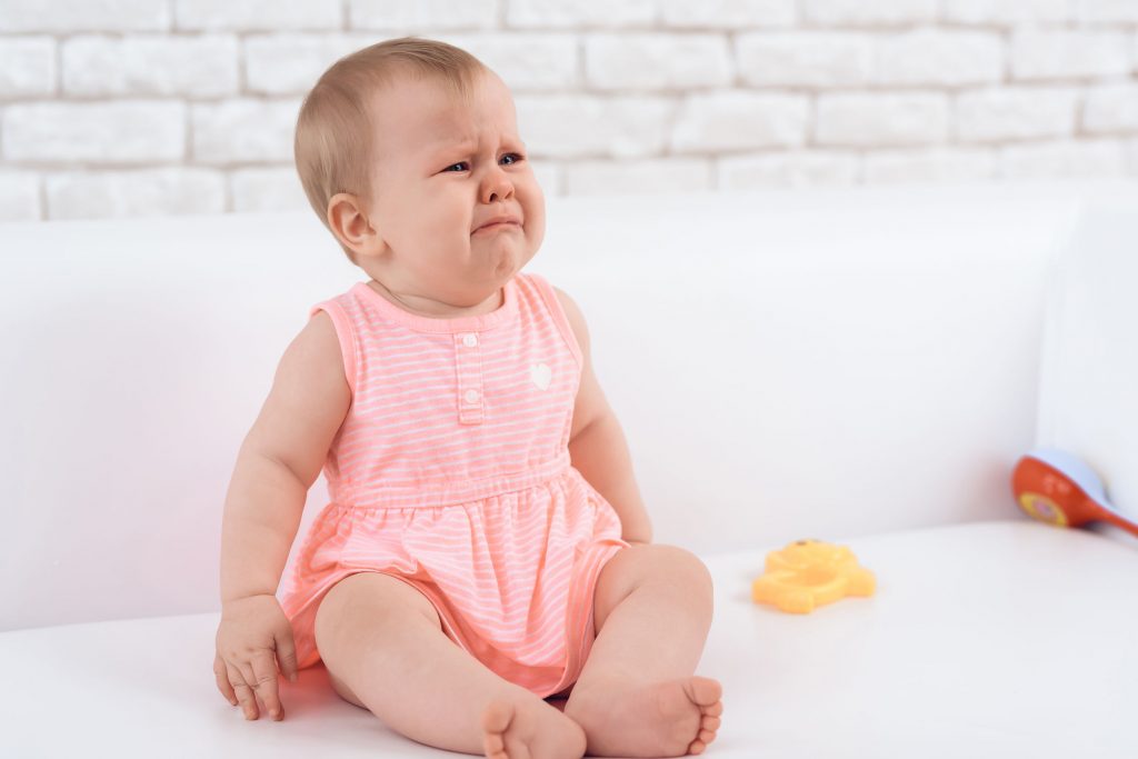 Little newborn baby pink dressed crying bitterly.