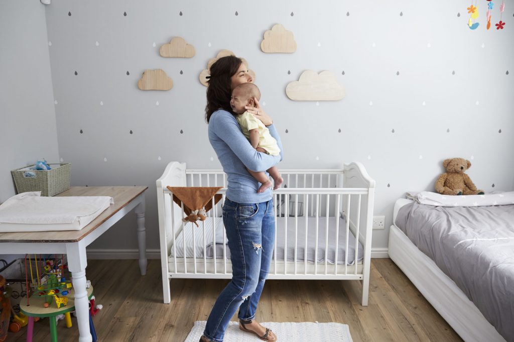 Mother Comforting Newborn Baby Son In Nursery