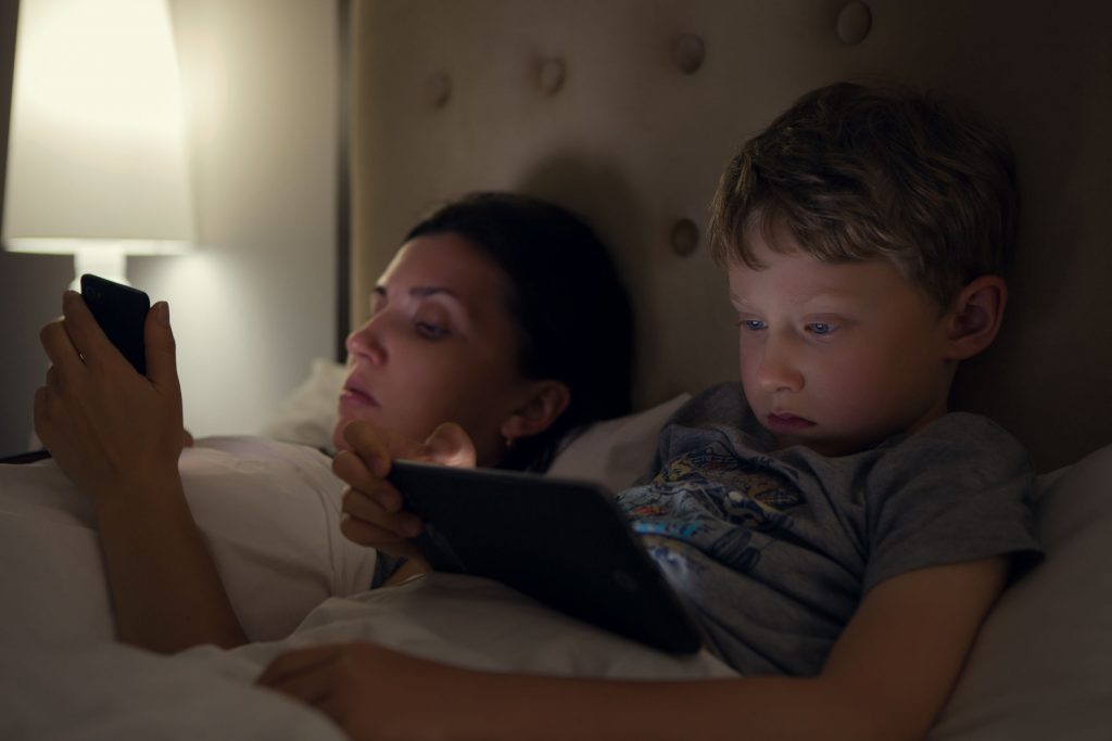 Mother with son looks in their electronic devices lying in bed