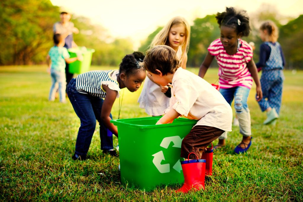 Group of children playing outside with a large recycling bin. 