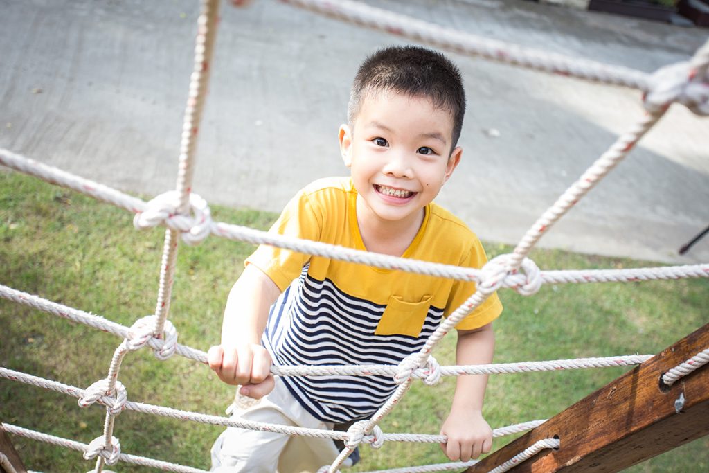 Little asian boy climbing rope obstacle activity on the playgrou